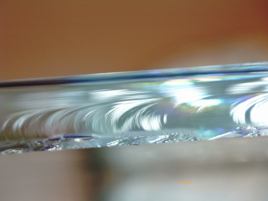 Wallner lines indicate the direction of fracture travel (to the left) and the surface with compressive stress (top) and with tensile stress (bottom). The lower edge is the coated side and points to the space between the panes; the fracture started from this surface.