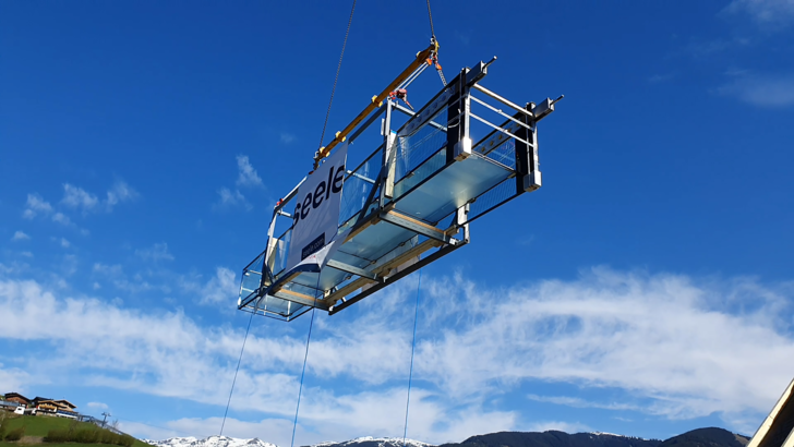 Floating: The glass walkway was lifted over the Bründl‘ Sports building to the installation site on the fourth floor with the help of a 45m long jib. - © seele
