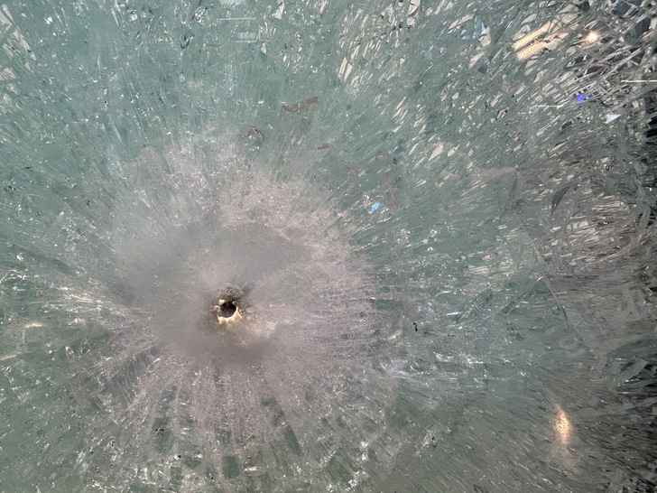 Close-up of damaged insulating glass with a central impact point that creates a star-shaped crack pattern, relevant for safety and resistance in window and façade technology.