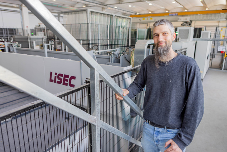 Man with long beard in an industrial facility, standing near machinery with "LiSEC" logo. - © Lisec