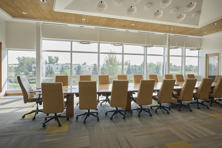 Spacious conference room with a long table, leather chairs, and large windows overlooking greenery. - © SageGlass