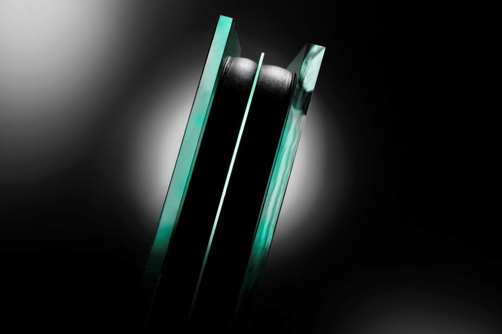 Close-up of layered glass panels with a black material in between, set against a dark, gradient background. - © Glaston