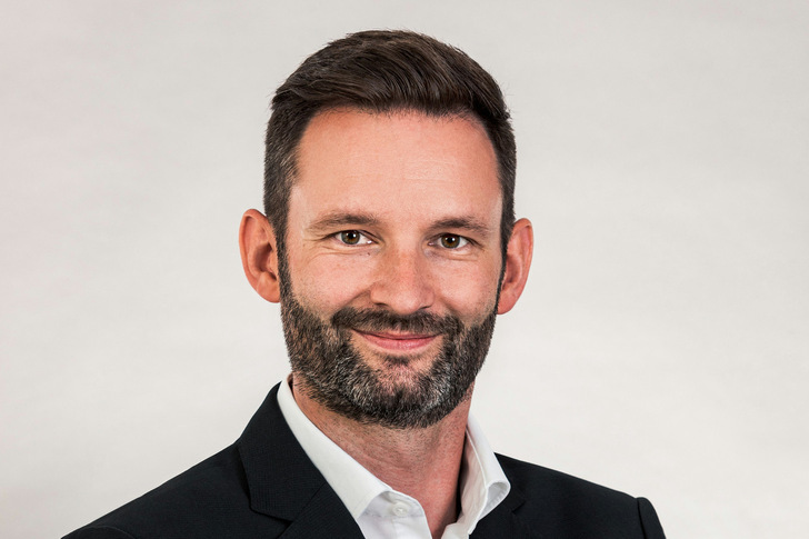 Smiling man with dark hair and beard wearing a suit jacket and white shirt against a light background. - © Dengg engineering security