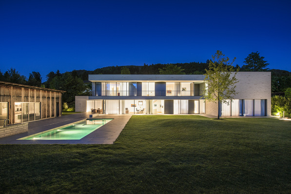 The rear façade of the elongated building structure opens out almost fully towards the garden on both levels by means of floor-to-ceiling sliding systems.
