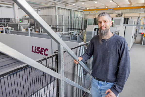 Man with long beard in an industrial facility, standing near machinery with "LiSEC" logo. - © Lisec