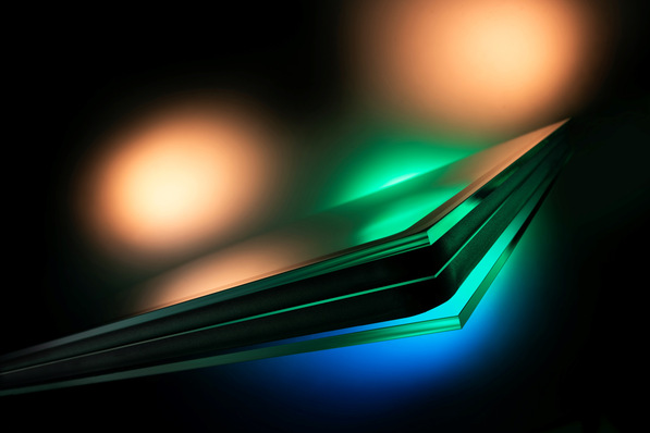 Abstract close-up of layered glass panels with green and blue lighting effects against a dark background. - © Glaston