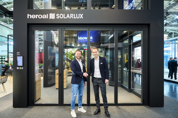 Two men shaking hands in front of a glass entrance with "heroal SOLARLUX" signage above. - © Solarlux