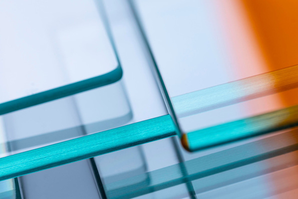Close-up of overlapping glass sheets with blue and orange reflections, creating abstract geometric shapes. - © Glaston